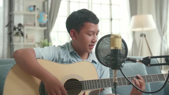 Asian Boy Vlogger Playing Guitar And Sing A Song. The Child Is Broadcasting Live On The Internet