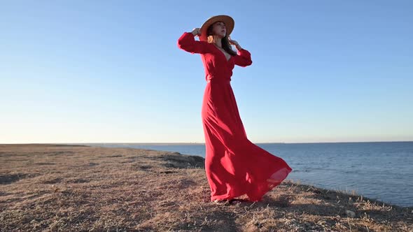 A Romantic Woman in a Red Dress Stands on the High Seashore