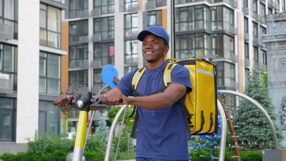 Smiling Afroamerican Man Courier Delivery Walks Street with Electric Scooter