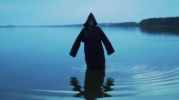Evil witch in black cloak with hood in the river. Halloween costume.