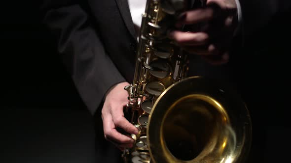 Musician in formal suit plays shiny saxophone with hands in the studio, close-up on black background