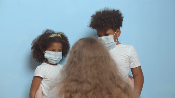 Back View of Caucasian Woman Embracing African Boy and Girl in Protective Mask