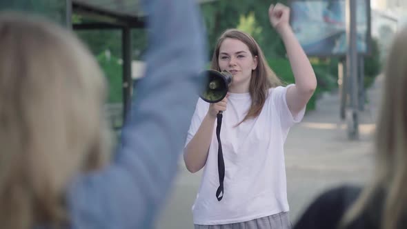 Portrait of Protest Leader with Megaphone Encouraging Crowd with Banners. Young Caucasian Woman