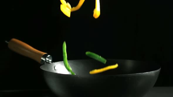 Mixed peppers falling into a wok on black background