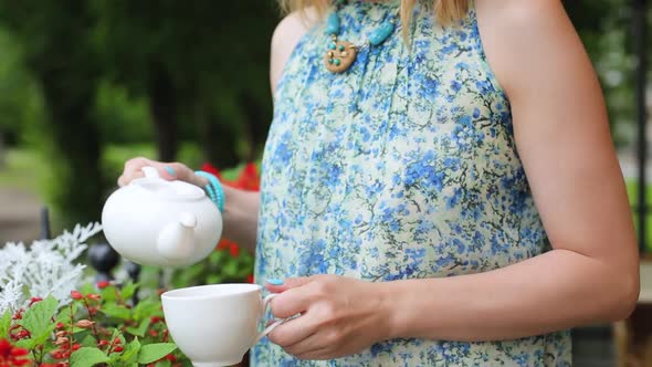 Woman in a Summer Cafe Pours Tea Into a Cup Close-up Standing. Woman Stands on the Background of the