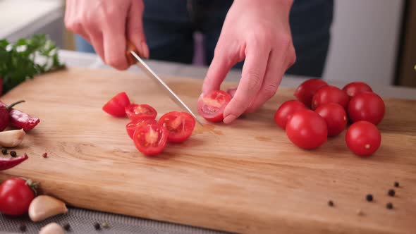 Woman Cutting Fresh Cherry Tomatoes with Kitchen Knife on Wooden Cutting Board