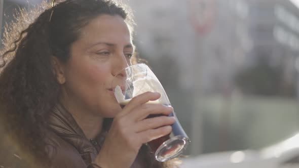 Attractive curly hair woman smiling and drinking a glass of beer on a beautiful sunny day.