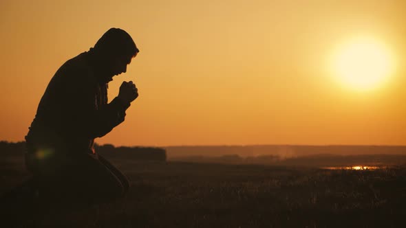 Silhouette Young Man Praying Outside at Beautiful Sunset. Male Asks for Help Finding Solace in Faith alt