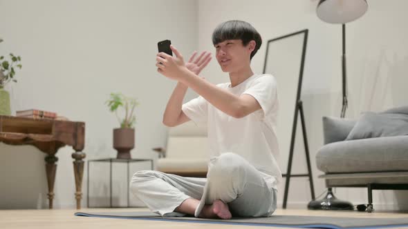 Asian Man Talking on Video Call on Smartphone on Yoga Mat