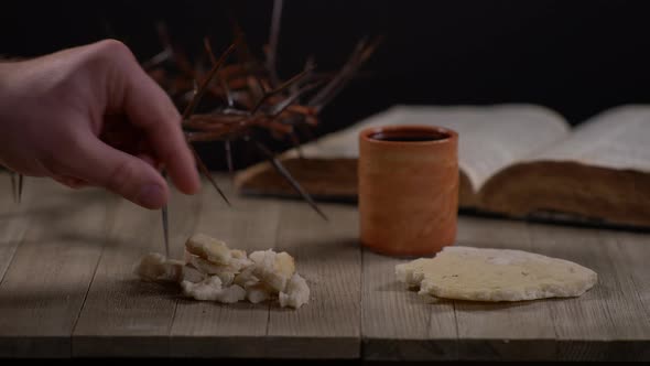 Ripped Bread Being Placed On Table Surrounded By Bible, Wine And Crown