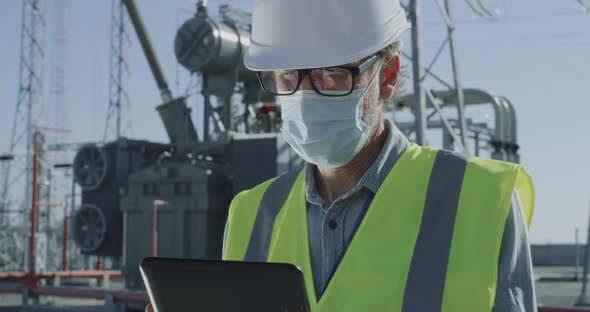 Male Engineer in Mask Using Tablet on Power Station