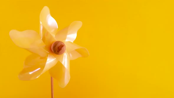 One yellow plastic pinwheel windmill spinning fast on the left on vibrant yellow blurred background