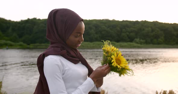 Black Muslim Woman Holding Flowers While Standing Near Lake