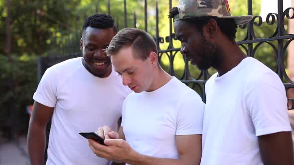 Three Multiracial Students Communicate with Each Other, Look at the Phone and Laugh