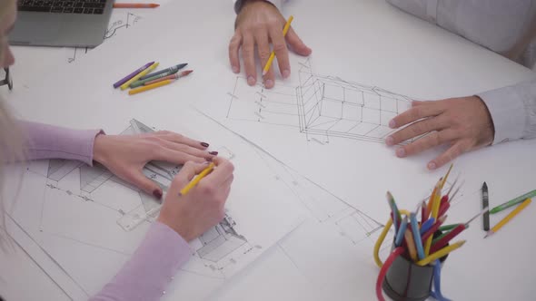 Top View of Two Caucasian Architects Drawing Blueprints at the Table