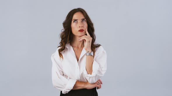 Woman in White Shirt Has Folded Hands and Looking Thoughtful Smiling and Raising Forefinger Up Like