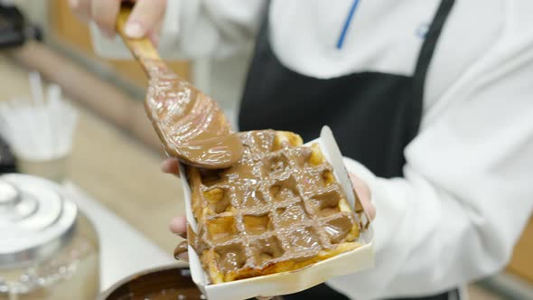 Hand Of Woman Pouring or Smudging Chocolate Over Waffles with a Wooden Spoon at Night