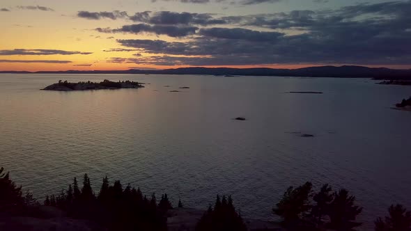 Reveal of Rocky Pine Tree Island in Big Lake just after Sunset, Drone Aerial Wide Dolly Out. Colorfu