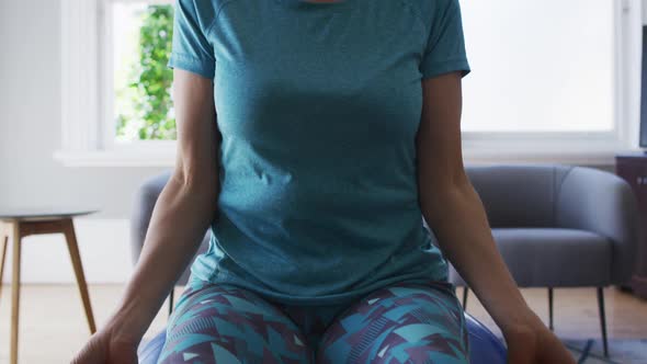 Caucasian senior woman exercising with dumbbells while sitting on the gym ball at home