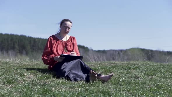 Woman sketching in a park sitting on the short green grass under the summer sunlight