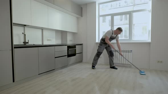 A Builder in Uniform Washes the Floor in a New Apartment