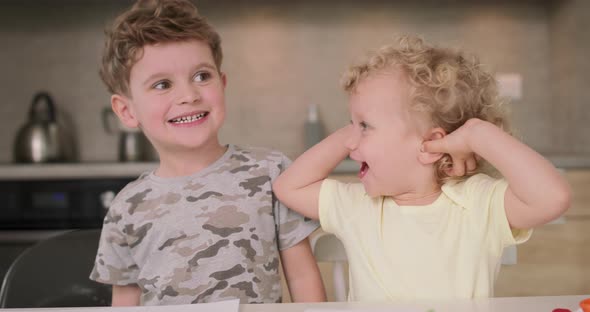 Adorable Brother and Sister Smile and Laugh Together While Sitting at the Kitchen Table Girl Touches