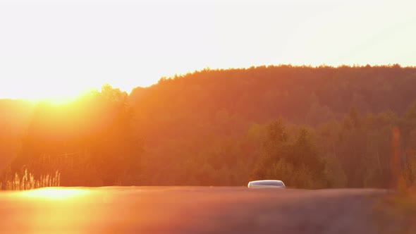 The Car Drives Out From the Horizon Against the Backdrop of the Evening Sun