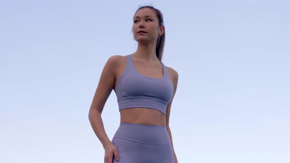 Beautiful Asian woman adjusts athletic wear while posing, Slowmo Low Angle