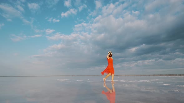 Portrait of a Young Woman in a Fluttering Dress. Girl Traveler Walks on a Pink Salt Lake