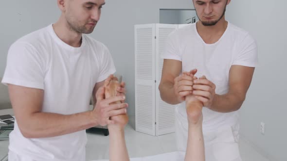 Two Male Massage Therapists Doing Massage of the Legs of a Young Girl