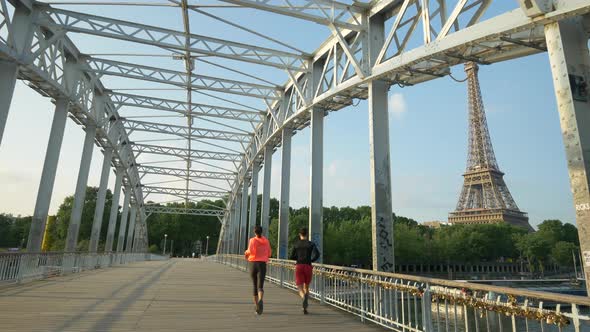 A couple running across a bridge with the Eiffel Tower