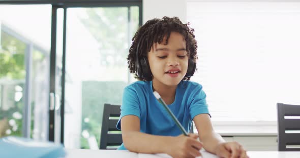 Happy biracial boy sitting at table in kitchen doing homework