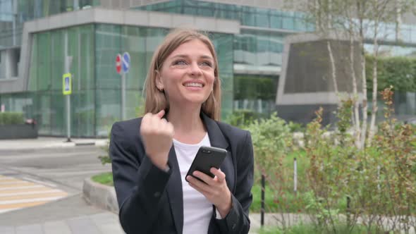 Businesswoman Celebrating Success on Smartphone While Walking on the Street
