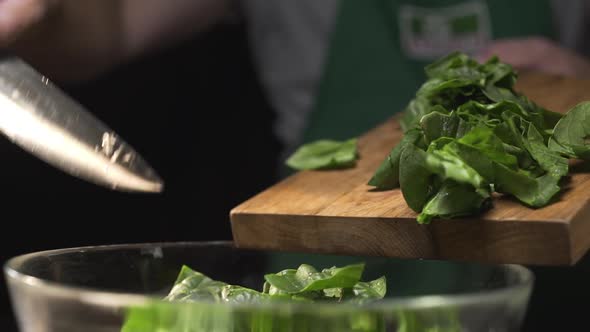 The Cook Pours Chopped Spinach From the Cutting Wooden Board To the Glass Bowl