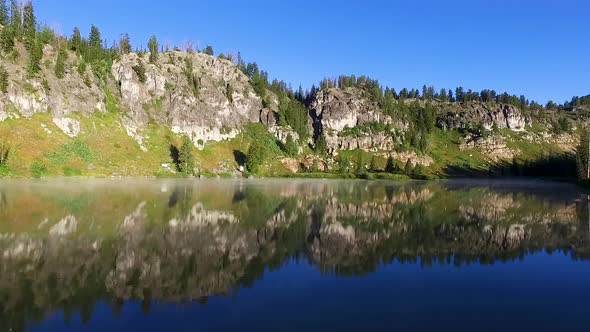 Panning view of a high mountain lake with the mountains and forest reflecting off the glassy surface