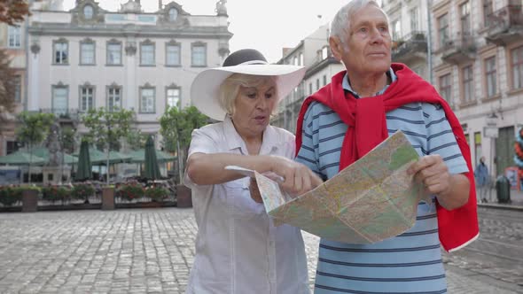 Senior Male and Female Tourists Walking with a Map in Hands Looking for Route