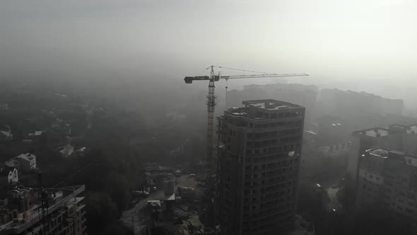 Birds eye view on tower crane in fog standing next to residential building.