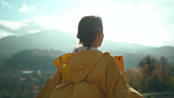 Joyful Freedom Girl in Yellow Jacket Standing with Open Arms Around Mountains and Hills Sun Lights