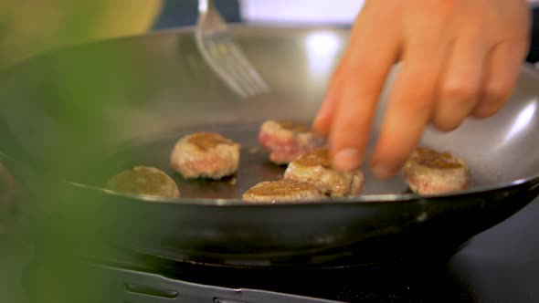 Small size juicy meat balls frying in a steel pan, chief checks both sides, handheld close up shot