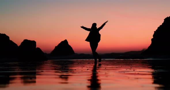 Happy Excited Woman Dancing on Ocean Beach in Cinematic Pink Orange Sunset Light