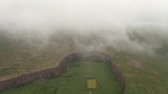 Drone Ascend Over The Clouds And Fog With Asbyrgi Canyon In Iceland. - aerial