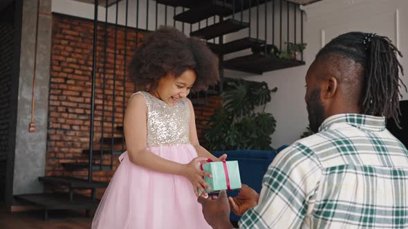 Beautiful Little African American Birthday Girl in Pink Dress Getting Gift Box From Her Father and