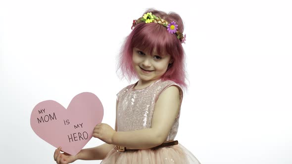 Child Girl Princess Holds Pink Paper Heart with Text About Mother. Mother's Day