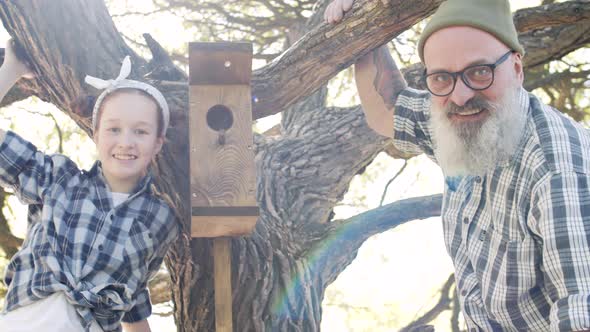 Aged Man and His Granddaughter near Birdhouse