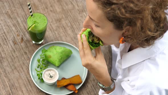 Top View of Young White Woman Takes a Bite of Her Delicious Vegan Burrito Served with Sauce a Side