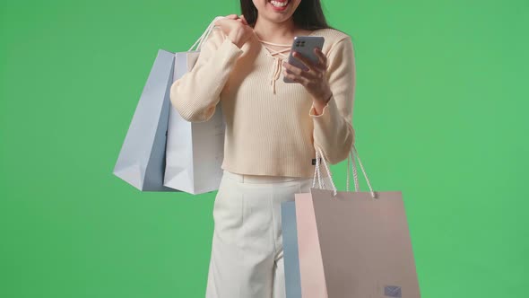 Woman Holding Shopping Bags Use Mobile Phone And Smile While Walking In Front Of Green Screen