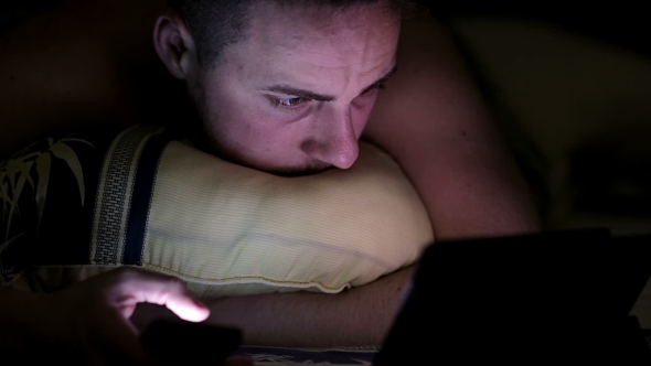Young Man With Tablet And Smartphone In Bed At Night