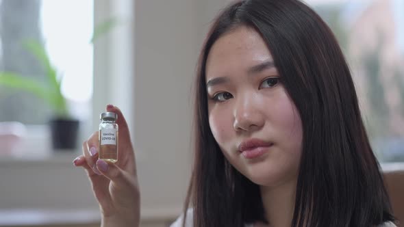 Closeup Portrait of Young Asian Woman Holding Covid19 Vaccine Jab Looking at Camera