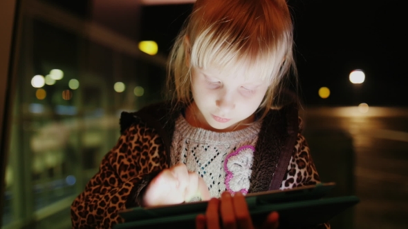 A Girl Enjoys The Tablet On The Background Of a Large Window With Reflections