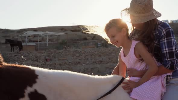 Happy family mother and daughter having fun riding horse inside ranch at sunset